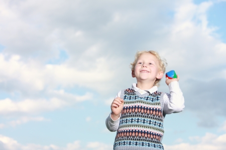 Low angle view against a cloudy sky of a happy little boy throwing a colourful ball with copyspaceの写真素材