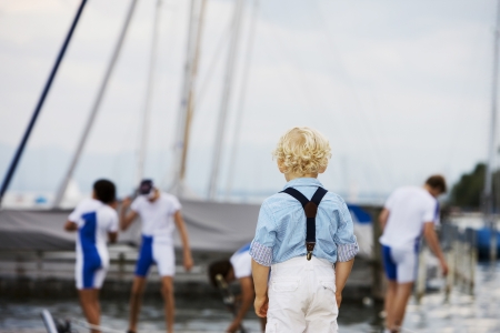 Little boy with curly blonde hair standing with his back to the camera watching his favourite sports teamの写真素材