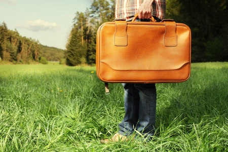 Man with vintage travel bag standing on green lawn - travel conceptの写真素材