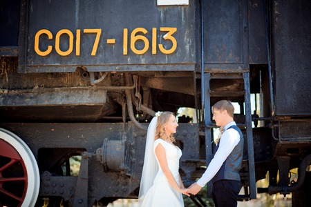 Beautiful Bride in Wedding Dress and Groom Just Married Kissing near Trains on Railroad. Honeymoon Travelの写真素材