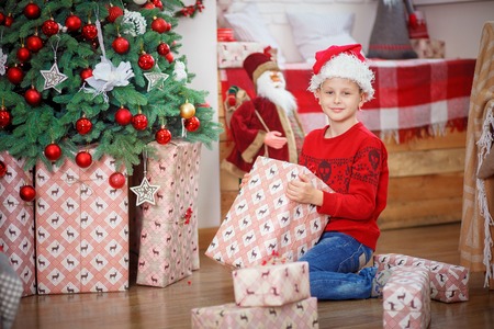 Very happy cute Boy with xmas gifts on wooden background. Child in santa hat. Happy christmas and new year holidays. Space for text. Boy in plaid shirt and suspenders. New Year and Christmas treeの写真素材