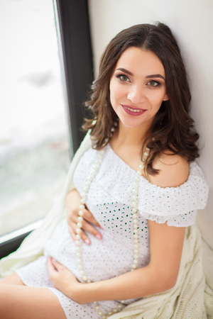 Pregnant woman standing near window with baby's bootees in the roomの写真素材