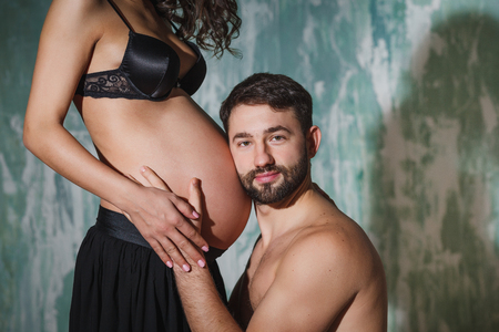 Man listening to belly of happy pregnant wife on bed at homeの写真素材