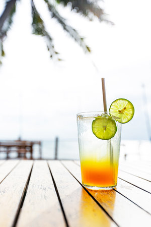 Cocktail with lime and straw on a wooden table by the seaの写真素材
