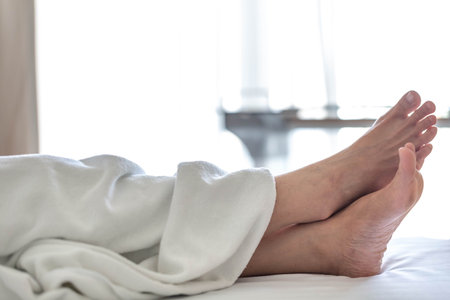 Close-up of a woman's legs in a white bathrobe lying on the bed at home