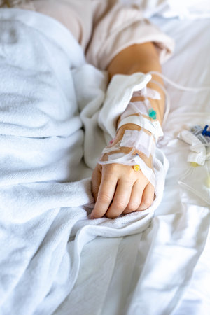 Close-up of patient's hand with saline intravenous (IV) on the bed.の写真素材