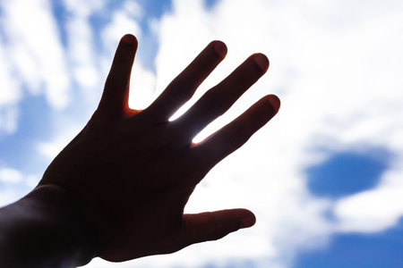 Silhouette of hand on the blue sky background with white clouds