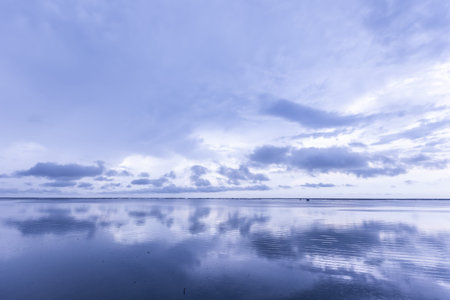 Blue sky with clouds reflected in the calm water of a lake.