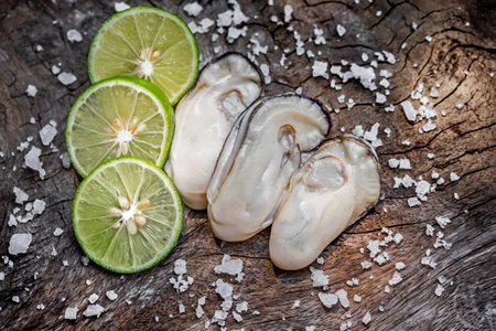 Fresh oysters with lime and salt on wooden background. Top view