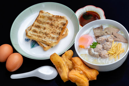 Rice porridge with pork, egg, bread and vegetables on black background
