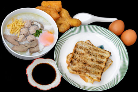 Rice porridge with pork and fried egg in white plate on black background