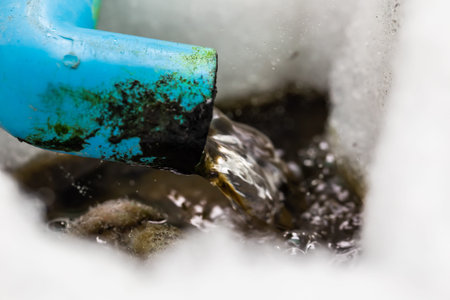 Close up of an old blue watering can pouring water into a stream.