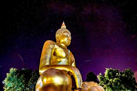 golden buddha statue at night with starry sky backgroundの写真素材