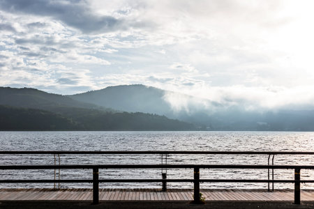 Wooden pier on the lake with mountains and fog in the backgroundの写真素材