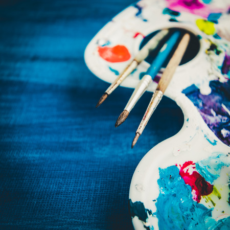 Creative background with art palette and brushes on blue painted canvas. Selective focusの写真素材