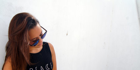 Young beautiful brunette woman with dark hair in a black dress and sunglasses on a white backgroundの写真素材