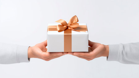 Two hands holding a gift box with a bow on a white backgroundの素材