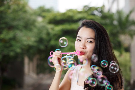 Asian female collegue student enjoying blowing soap bubbleの写真素材