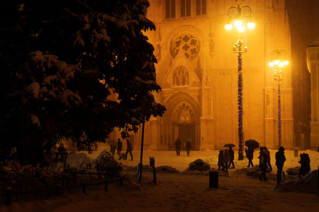 Zagreb, Croatia: January 6 1016: Cathedral of Zagreb in the night during christmastime snowing and orange light with people with umbrellas, Zagreb, Croatiaのeditorial素材