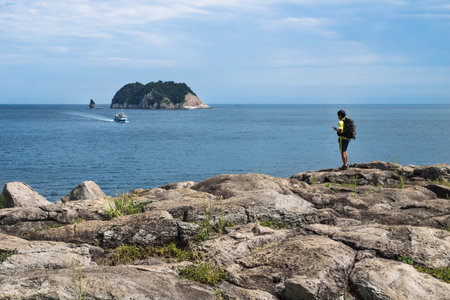 Seogwipo, Jeju Island, Korea - August 26 2017: Hiker on the cliff of Seogwipo looking to boat and Moon Islandのeditorial素材