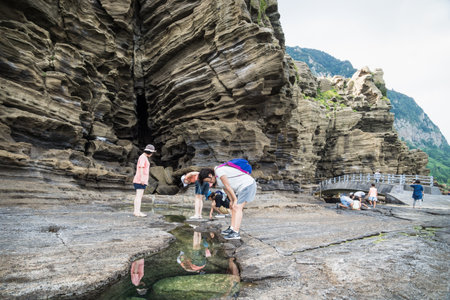 Yongmeori Beach, Sanbang-ro, Jeju Island, South Korea - August 28 2017: Tourist bowing and looking into green water pool for fishのeditorial素材