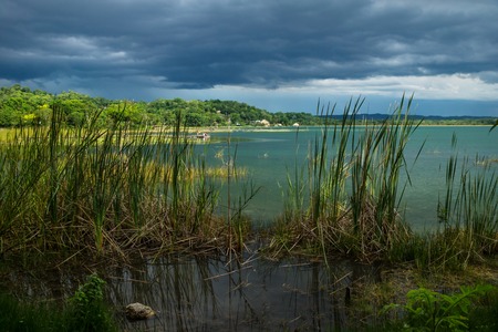 View on the dock behind grass along the lake shore with dark blue cloudscape and sunshine, El Remate, Peten, Guatemalaの写真素材