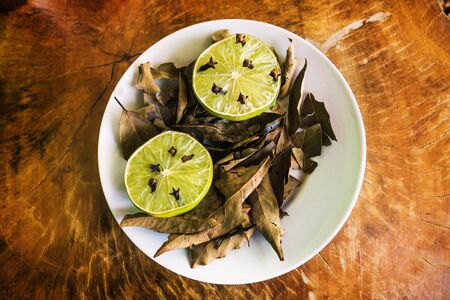 Natural repellent white plate with fresh lime, cloves and dried laurel on wooden table