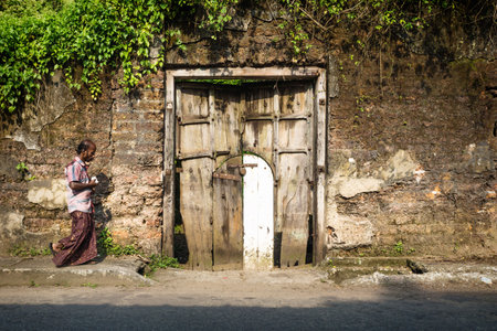 Kochi, India - 10 November 2017: Indian local man walking along abandoned sunshined wall with efeu and doorのeditorial素材