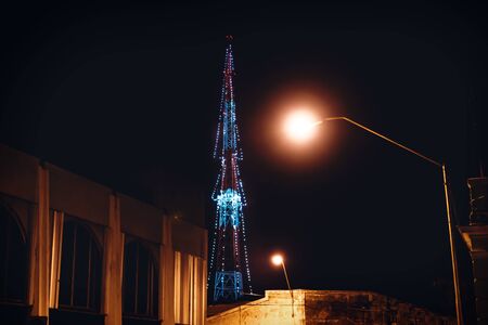 Transmitter tower decorated with lights as christmas tree with colonial building and street lights,...