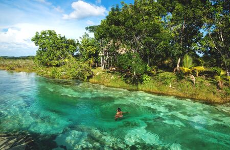 Man in rapids at sunny seven colored lagoon surrounded by tropical plants in Bacalar, Quintana Roo, Mexicoの写真素材