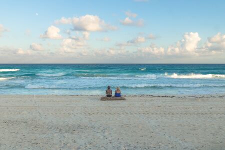 Two women sitting on a tree at the ocean with turquoise water during sunset at Cancun, Yucatan,...