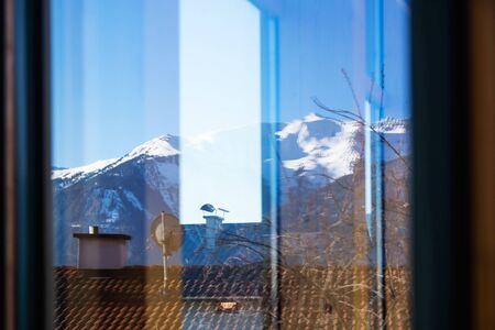Tyrolean Alp Quarantine window view with roofs and snow topped mountains, Austria