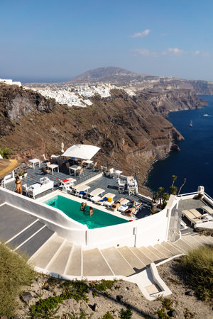 Imerovigli, Santorini, Greece - 20 July 2014: Guests at a hotel pool overlooking the high cliffs and village of Fira on a cloudless sunny dayのeditorial素材
