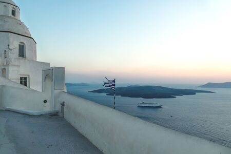 Purple blue sunset along sea coast with greek flag and cruise ship with view on blurred ocean and islands, Fira, Santorini, Greeceの写真素材
