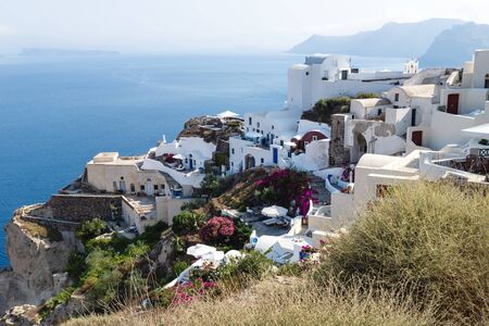 Traditional white washed Greek houses along the coastline with blue ocean in Oia, Santorini, Greeceの写真素材