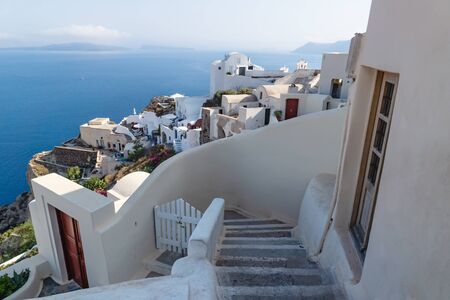 Stairs down to traditional white washed Greek houses along the coastline with blue ocean in Oia, Santorini, Greeceの写真素材