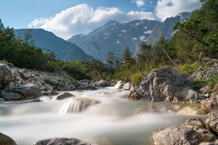 Clear river in long exposure with forest and Austrian Alp Mountains on a sunny day, Mieming, Tyrol, Austriaの写真素材