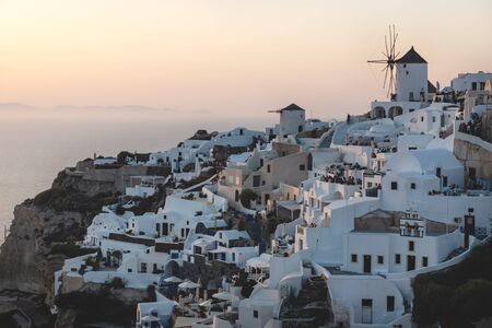View on Greek village with white wind mill on cliffs along the ocean during sunset, Oia, Santorini, Greeceの写真素材