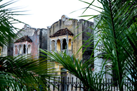 Colorful abandoned colonial houses with balconies behind blurred tropical palm trees, Merida, Yucatan, Mexicoの写真素材