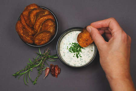 Arial view eating spicy sweet potato chips garnished with chili, rosemary and thyme and yogurt garlic chive dip sauce in black bowlsの写真素材