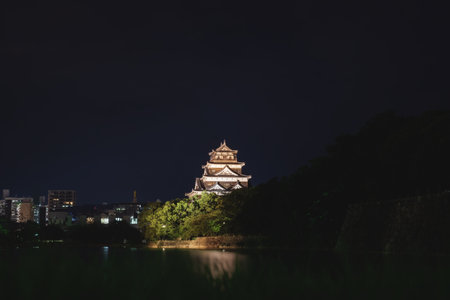 Hiroshima, Japan - September 15, 2017: The illuminated Hiroshima castle, also called Carp Castle, surrounded by water with reflections in the cityscape at nightのeditorial素材