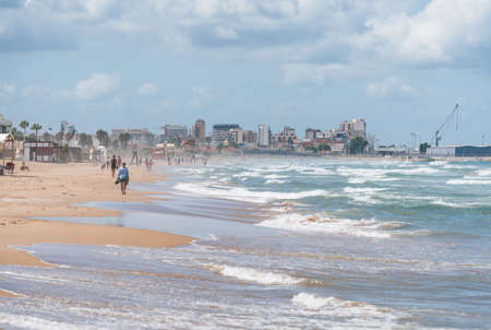People playing and walking on sunny sand beach with high ocean waves in Daimus, Spain