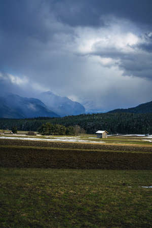 Melting snow on agricultural winter field with view to the foggy valley with dramatic cloudscape, Mieming, Tirol, Austriaの写真素材