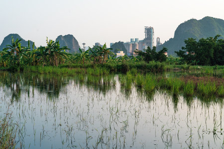 Huge cement factory settled between karst mountains in idyllic landscape along pond with banana trees in Ninh Binh, Vietnamの写真素材