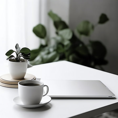 Close up view of simple workspace with laptop, notebooks, coffee cup and tree pot on white table witの素材