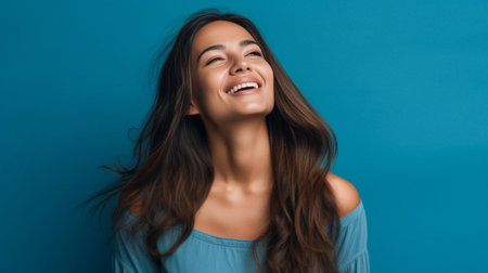 Happy young woman holding hands in hair and smiling while standing against blue background : Generative AIの素材