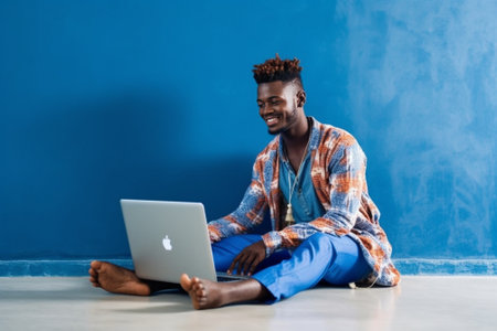 Happy man Handsome young man listening music and using computer while sitting on the floor against grey background : Generative AIの素材