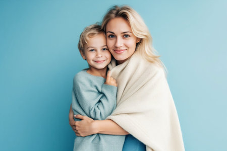 Portrait of adorable blond blueeyed baby boy looking at the camera with happy smile sitting on his mothers laps in pajamas Young beautiful woman spending morning with her : Generative AIの素材