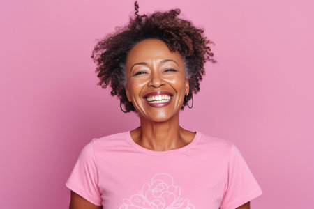 Pretty curly African American woman confesses in love makes heart gesture shows her true feelings has happy expression wears casual red t shirt poses over pink background : Generative AIの素材