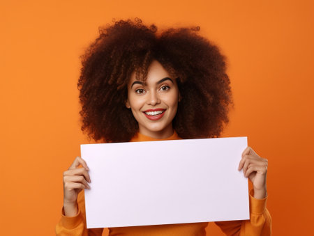Beautiful curly haired Afro American woman suggests to clickon link points on blank copy space shows way stands over white background wears basic orange jumper People and : Generative AIの素材